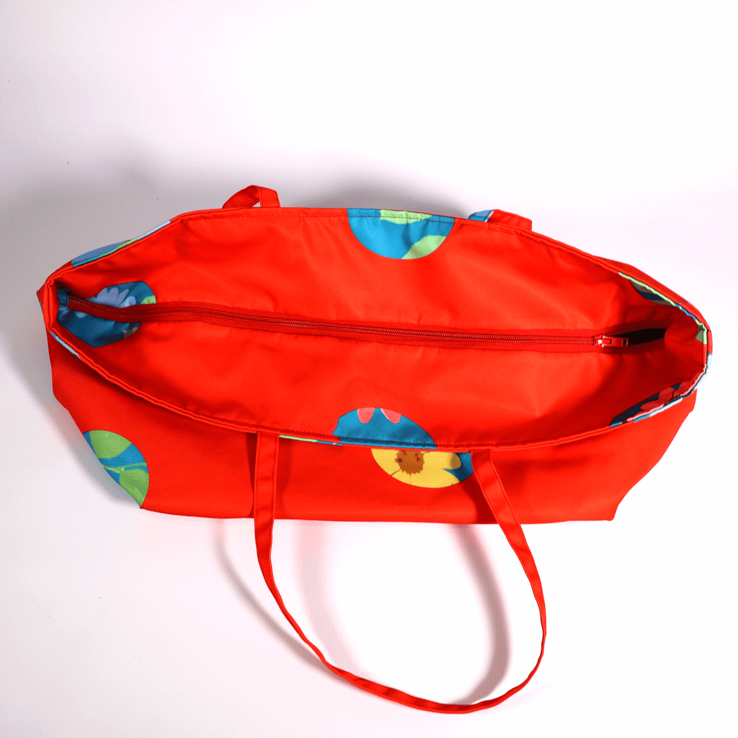 A bright red carryall bag with a stripe abstract floral design. Top view. Closed.