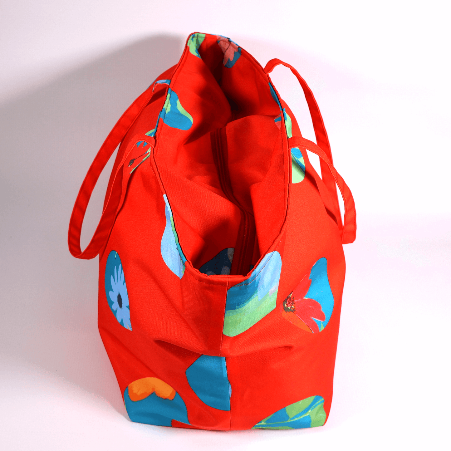 A bright red carryall bag with a stripe abstract floral design. Top view. Closed.