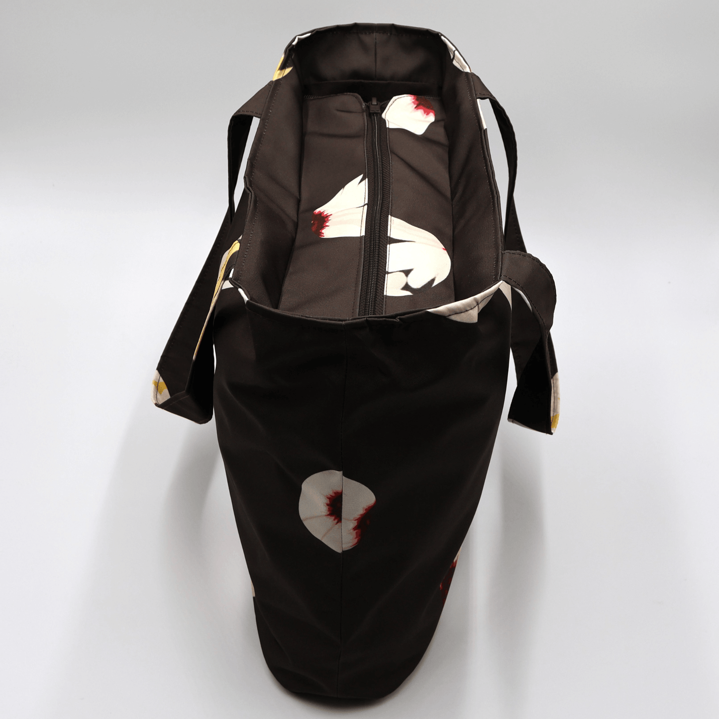 Shoulder bag with white abstract daisy design on a black background. Perfect for carrying books and documents. Top view.