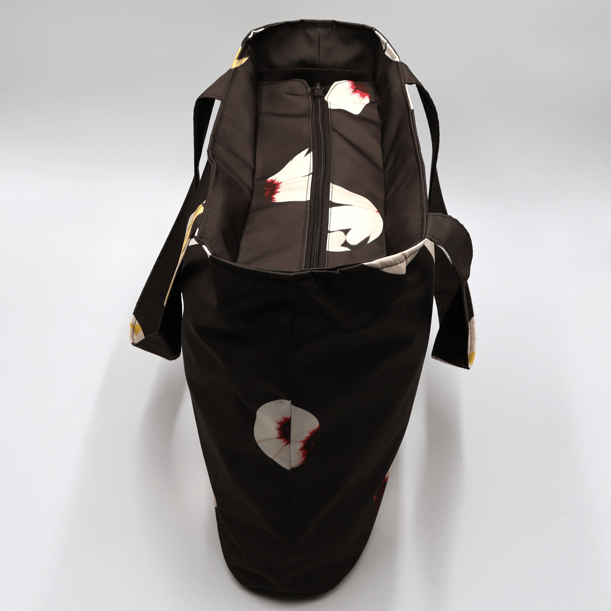 Shoulder bag with white abstract daisy design on a black background. Perfect for carrying books and documents. Top view.