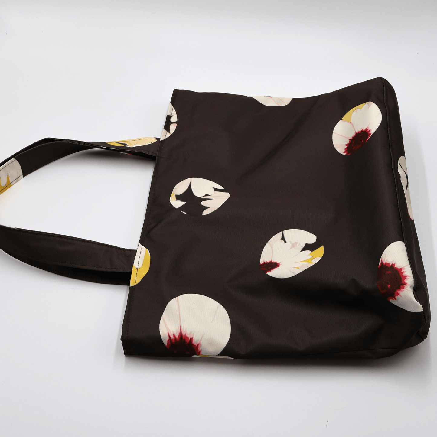 Shoulder bag with white abstract daisy design on a black background. Perfect for carrying books and documents. Flat view.