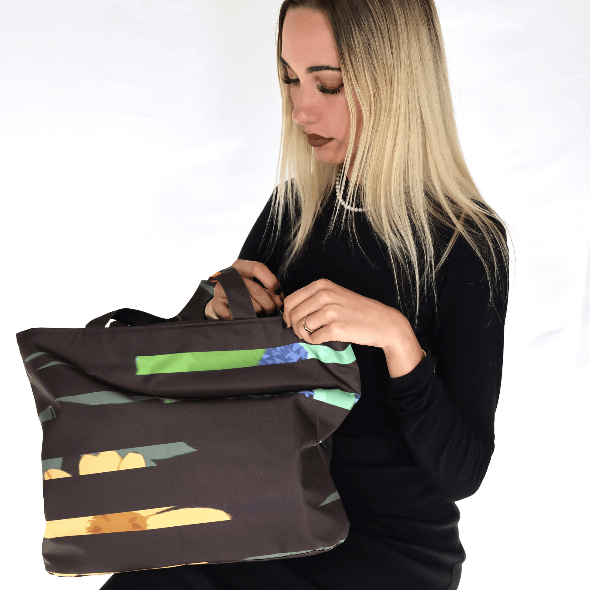 Model with shoulder bag with bright stripe/floral daisy design on a black background. 