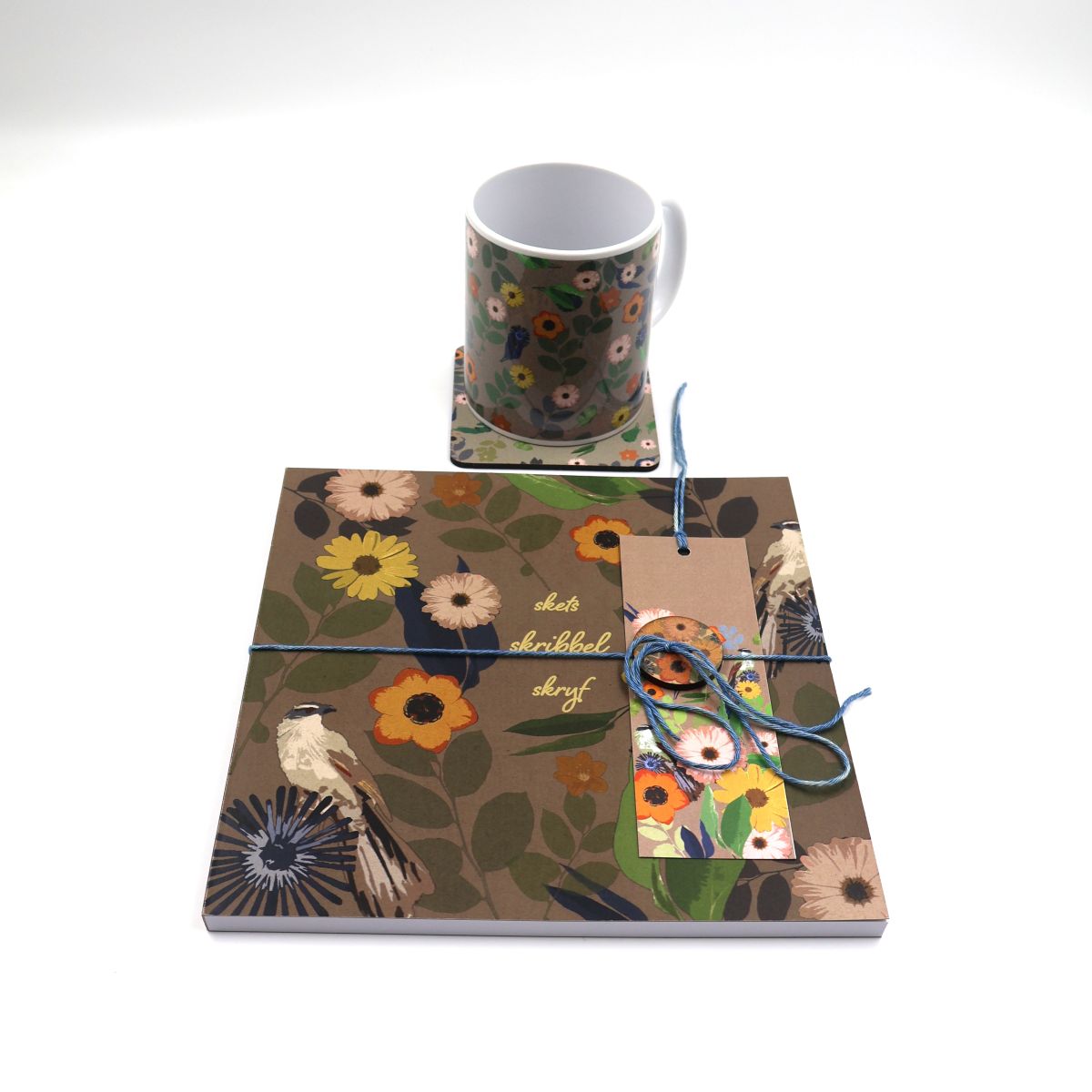 Handmade South African nature gift box neatly arranged with a square brown daisy sketchpad a matching ceramic coffee mug desk coaster and illustrated paper bookmark