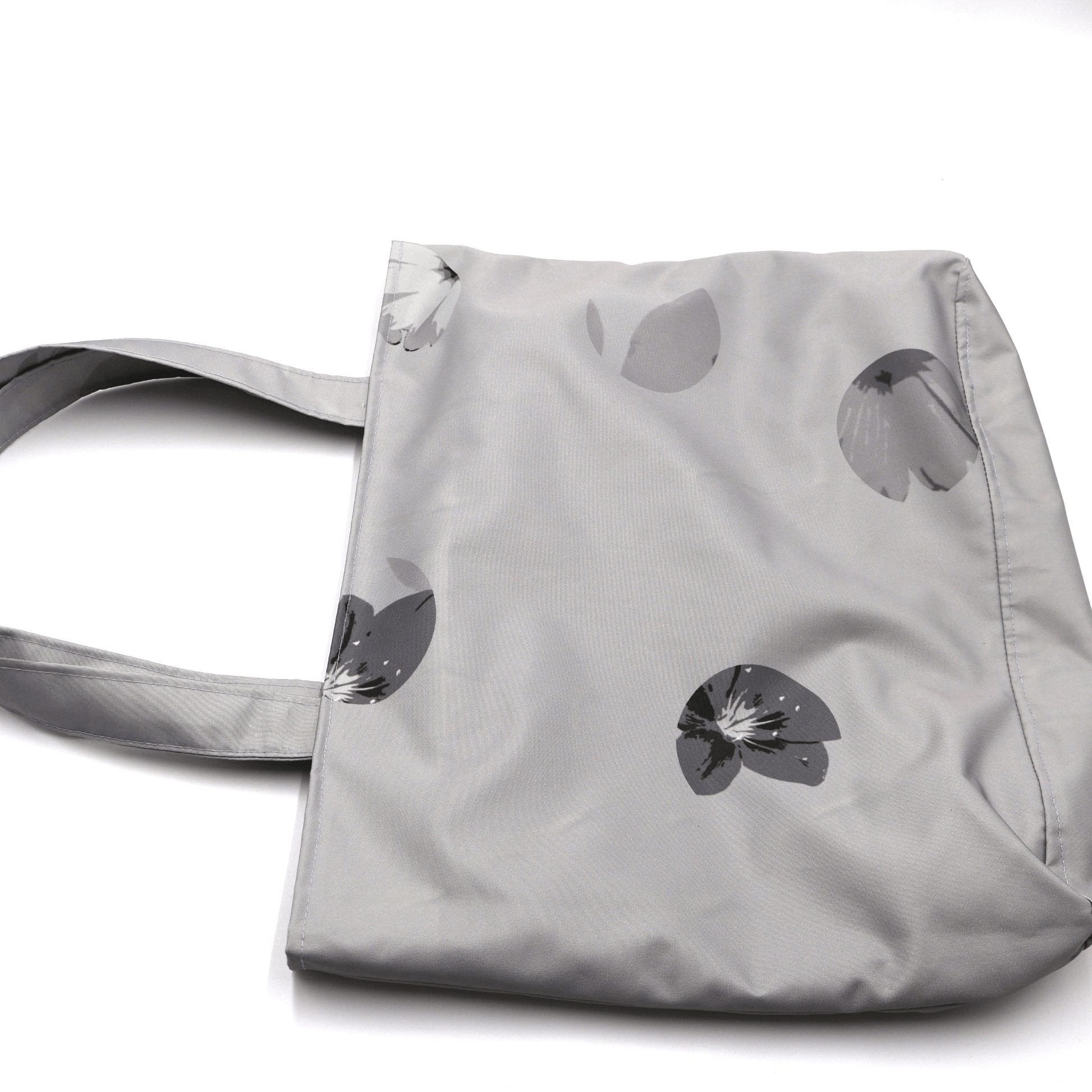Close-up of the Ellie B Grey Moon print on a canvas tote bag, showcasing the light grey and dark grey wind-blown petal surface design.