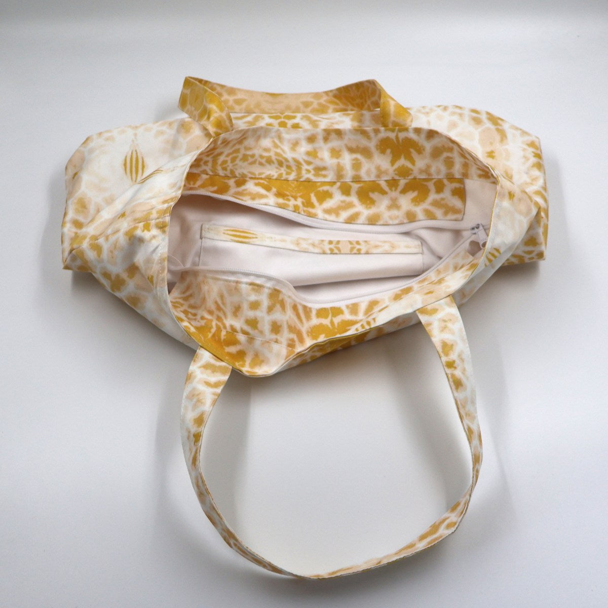 Flat lay view of Letheba butter yellow giraffe spot book bag showing secure top zipper closure