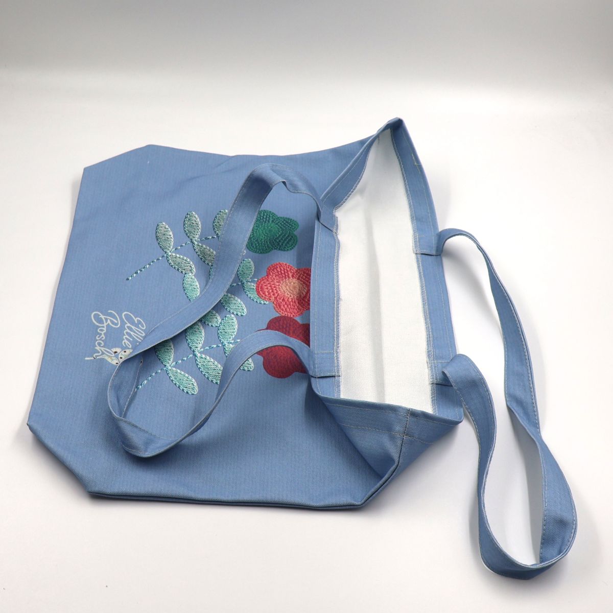 Close up view of a flat laid blue cotton canvas tote bag displaying the high quality neat stitching details along the handle seams