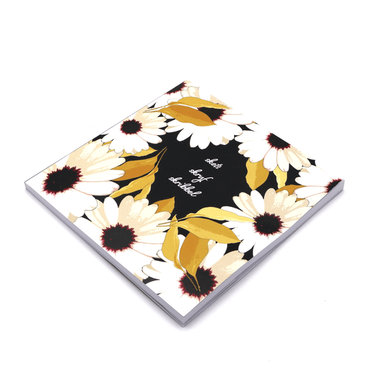 20cm x 20cm square blank notebook with a dramatic black background cover featuring a striking contrast print of white daisies and unique South African wildflowers